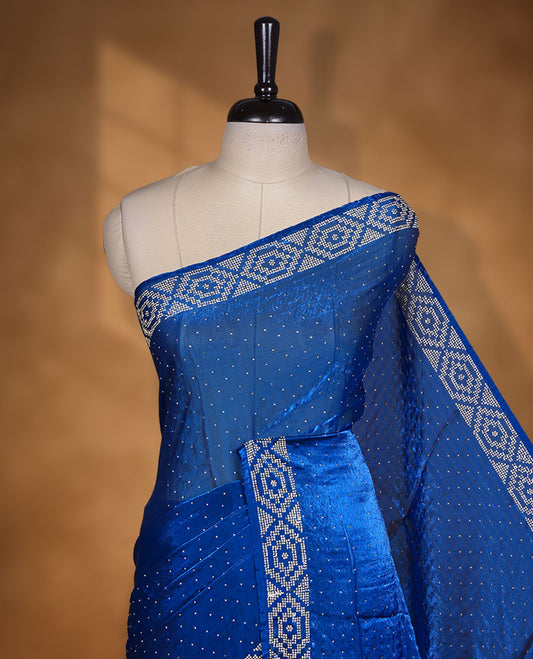 Royal Blue colour chiffon designer saree, featuring delicate scattered stone detailing all over the body, highlighted with intricate stone work and a heavy geometric stone pattern along the border and pallu, paired with a matching embellished blouse.a