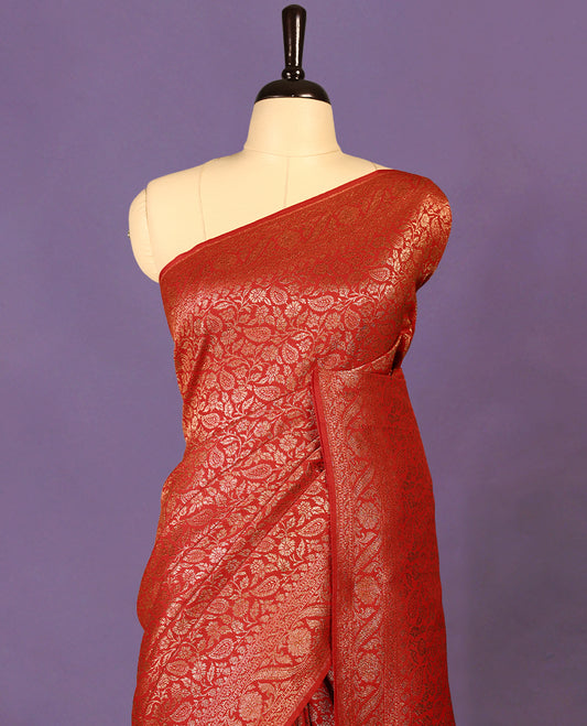 Chilli red colour semi Banaras Katan silk saree featuring intricate Antique Bronze zari floral and vine patterns woven throughout the body, enhanced with a rich traditional border and detailed pallu, paired with a matching blouse piece.