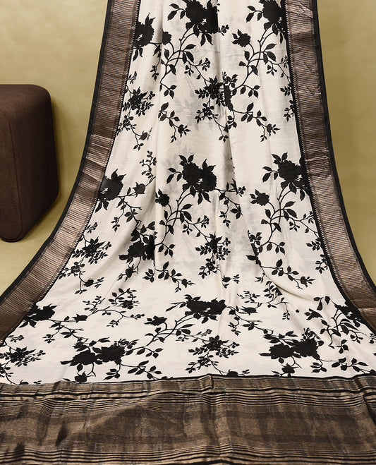 Off white colour viscose semi printed saree featuring a golden zari border, bold black floral vine prints across the body, and comes with a matching blouse