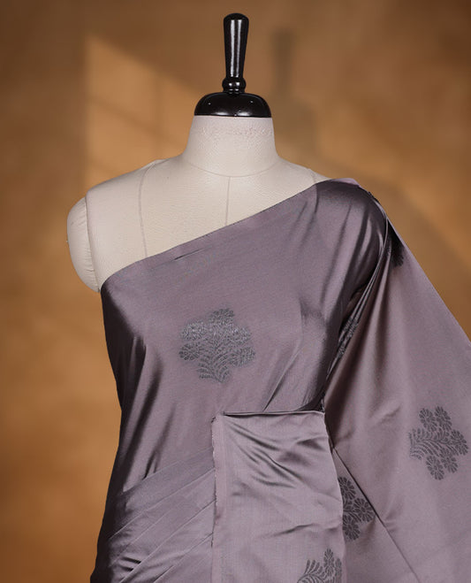 Reddish gray colour semi soft silk saree adorned with delicate woven floral motifs on the body, complemented by a contrast deep maroon colour woven pallu with intricate detailing and tassel accents without border & Comes with a matching blouse piece.