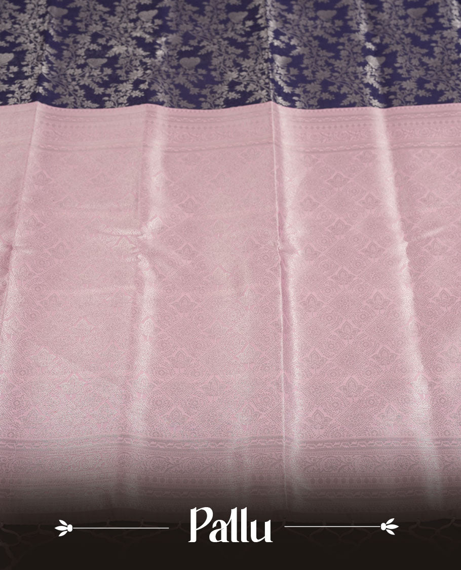 Navy blue colour semi silk saree adorned with subtle silver floral patterns on the body, complemented by contrasted a pastel light pink pallu intricately  woven with rich floral patterns border and pallu, and paired with a matching blouse