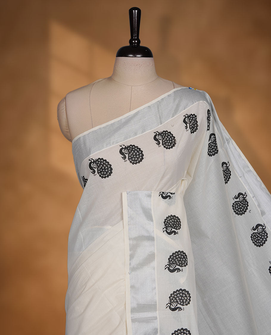 Off-white colour cotton Kerala saree featuring a subtle silver kasavu border, adorned with classic black peacock motifs across the body and pallu, and paired with a matching blouse.
