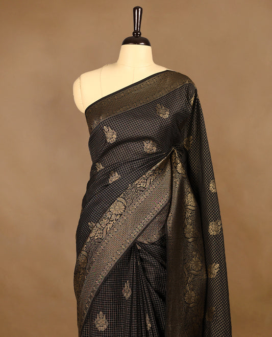 Black coloured semi Banaras georgette saree featuring golden Zari checks with floral motifs on the body, complemented by a self coloured traditional border with floral kodi design and a matching blouse.