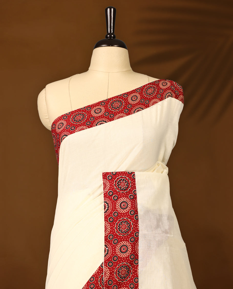 off white saree with a striking red printed border. The border features circular floral motifs in black and cream, with dotted detailing radiating outward, creating a traditional yet vibrant design