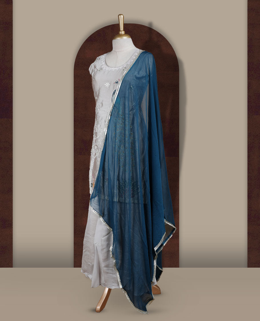 Elegant Ice grey colour embroidered sharara set featuring intricate peacock motifs and delicate stone detailing & Paired with a rich teal blue dupatta edged in silver and flared bottom.