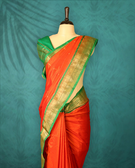 Deep Orange colour Traditional Kancheepuram Silk saree with small gold motifs on body, Green traditional border with intricate gold zari weaving, grand zari pallu, perfect for Bharatanatyam, with matching blouse.