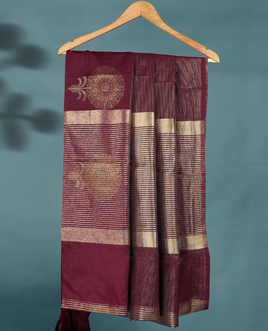 Dark Maroon Colour Semi Tussar Silk saree featuring golden zari horizontal lines across the body, adorned with bold floral motifs on the border, paired with a matching blouse.