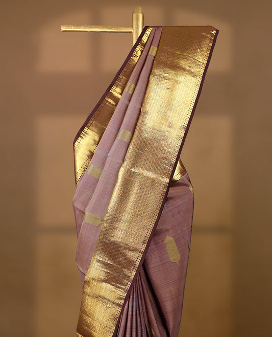 Muted mauve Colour traditional Kancheepuram silk saree adorned with antique zari traditional motifs on the body, featuring a contrasting border with Rich floral and geometric patterns, and paired with a matching blouse.