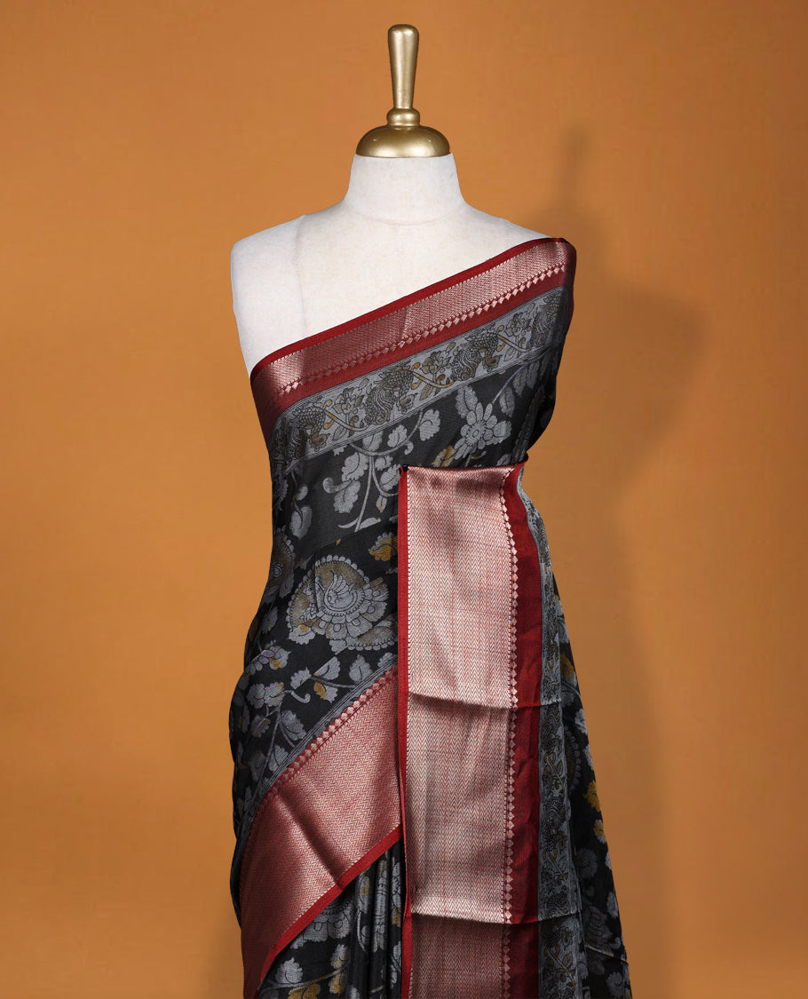 Black colour saree adorned with intricate floral motifs in subtle hues, featuring a rich maroon zari border and a beautifully woven contrasting pallu & Comes with a matching blouse piece.