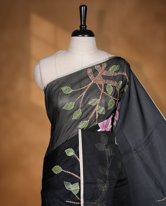 Black colour semi tusser silk saree featuring delicate floral embroidery motifs across the body with subtle contrast detailing on the border, paired with a matching embroidered blouse.