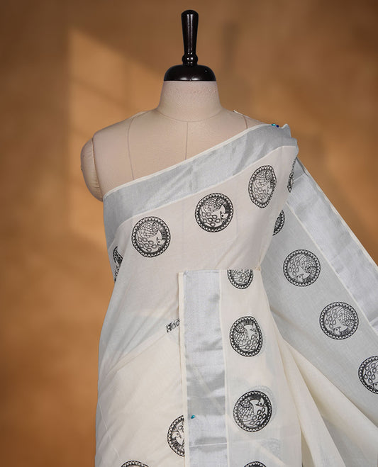 Off-white colour cotton Kerala saree featuring a subtle silver kasavu border, adorned with classic black cirlcle peacock motifs across the body and pallu, and paired with a matching blouse.