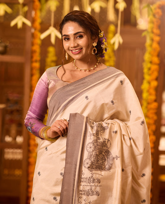 Off White colour Tussar saree adorned with small black woven motifs across the body, featuring an artistic temple chariot motif on the pallu, highlighted with a sleek grey border, paired with a matching blouse