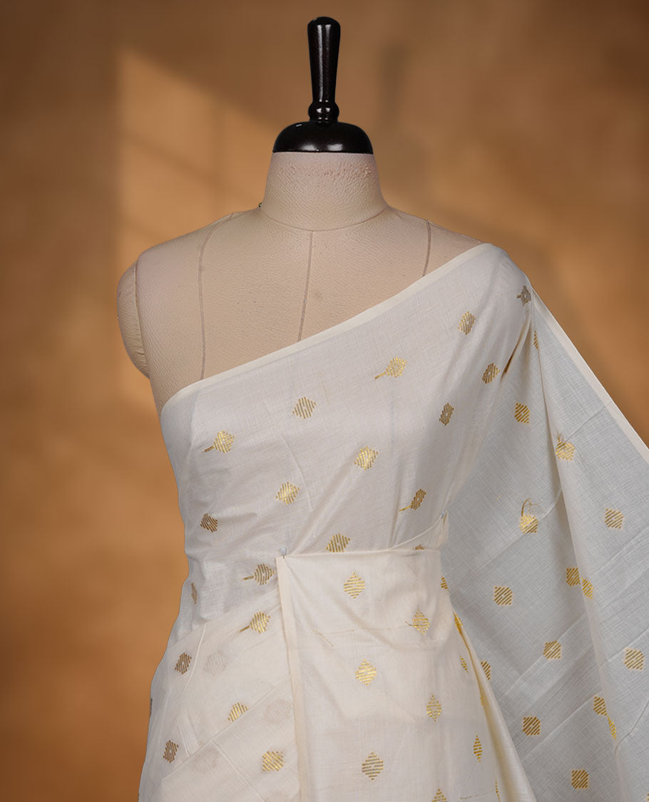 Off-white colour cotton Kerala saree featuring delicate gold butti motifs across the body and pallu, finished with a subtle gold border and tasselled pallu, paired with a matching blouse.