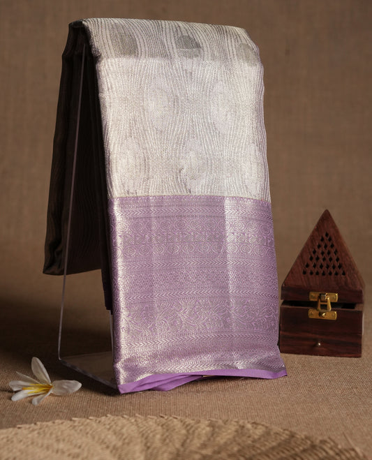 Pastel lavender Colour Kancheepuram tissue silk saree embellished with intricate silver zari work on the body, elegantly enhanced by a lavender traditional Chakkram and floral kodi design border, and paired with a matching blouse.