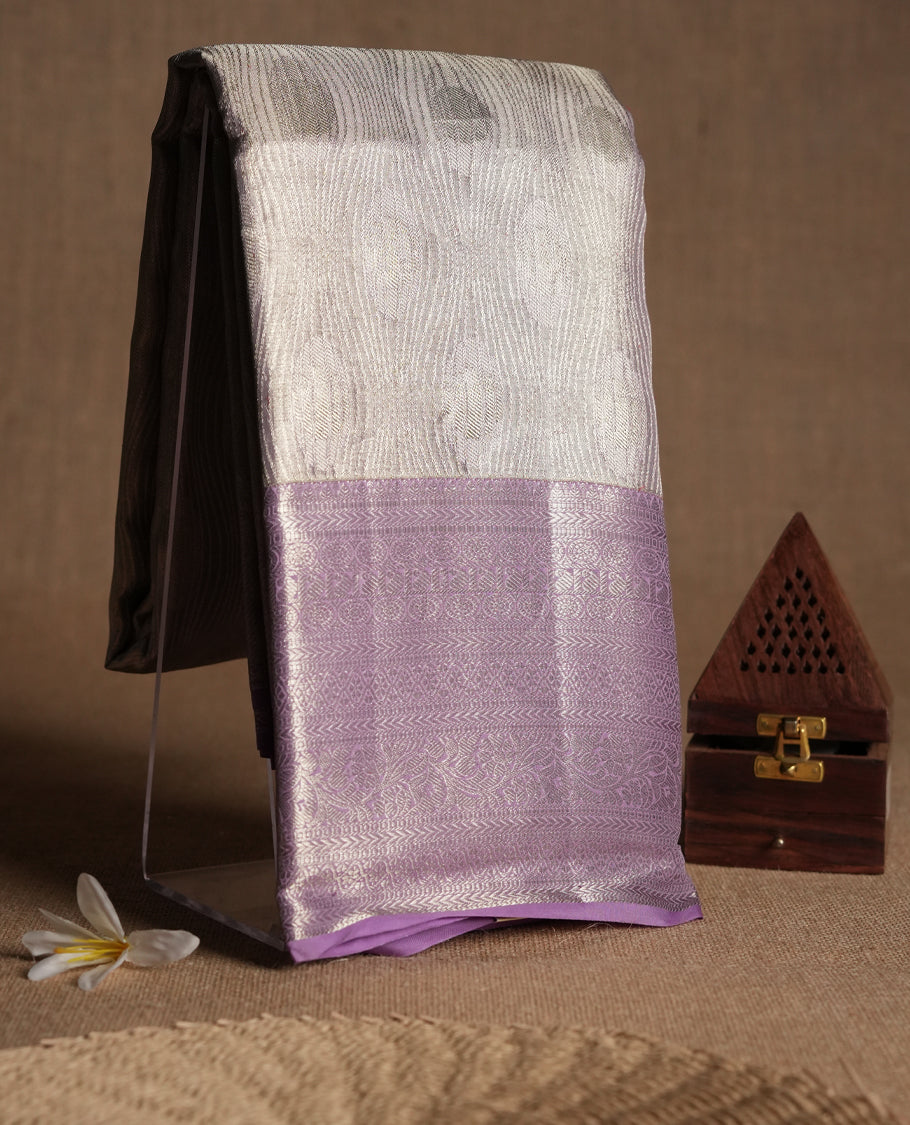 Pastel lavender Colour Kancheepuram tissue silk saree embellished with intricate silver zari work on the body, elegantly enhanced by a lavender traditional Chakkram and floral kodi design border, and paired with a matching blouse.