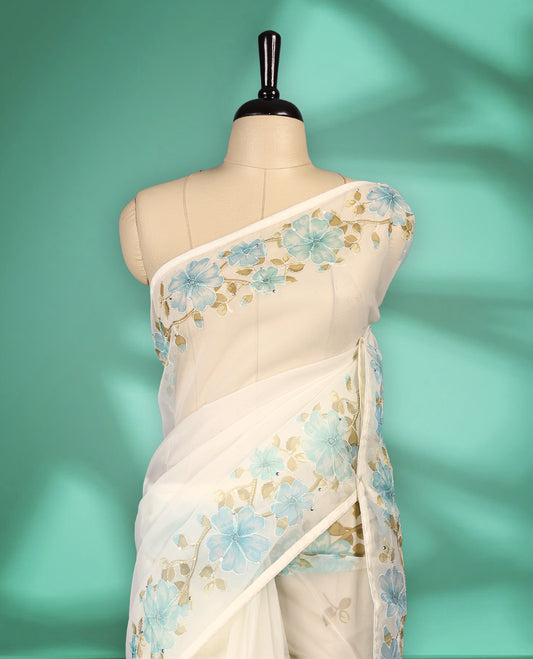 Ivory white colour organza saree adorned with aqua blue floral print with thread detailing on the border and pallu, in a sheer finish that adds elegance, paired with a matching blouse for a graceful look.