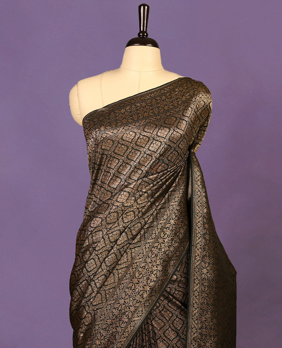 Black colour semi Banaras Katan saree featuring an antique Gold zari jacquard body, complemented by a self colour traditional border with a floral kodi design, paired with a matching blouse