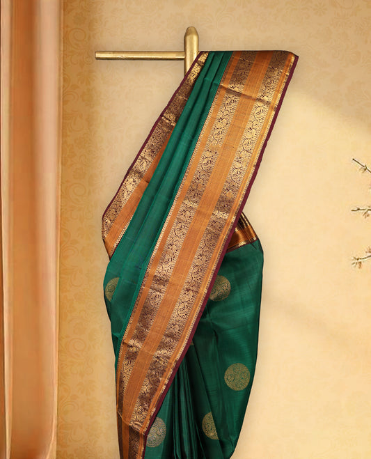 Bottle green pure Kancheepuram saree with gold zari Mayoora Chakra and diamond motifs on the body, contrast brown Kalakshetra border, grand pallu, and matching blouse.