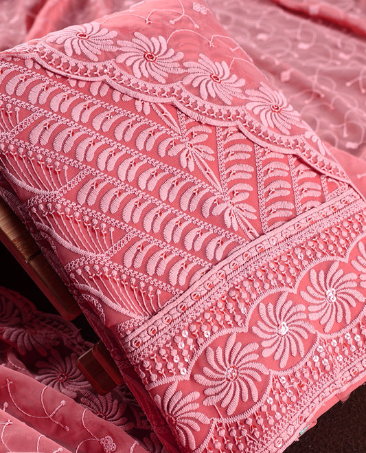 Charming coral pink churidhar material embellished with intricate floral embroidery and detailed thread patterns, paired with a plain matching bottom and embroidered dupatta, ideal for festive and elegant occasions.