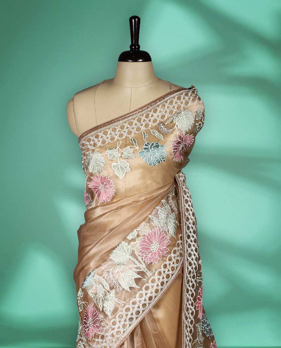 Light Brown colour organza designer saree featuring delicate pastel floral embroidery in pink, mint green, and white across the body, with a scalloped border accentuated by floral threadwork, and a gracefully embroidered pallu paired with matching blouse.