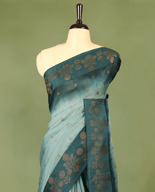 Sea green and teal double shade semi Banaras Tussar Georgette saree adorned with elegant antique gold zari floral motifs across the body, featuring a detailed woven border and grand pallu, paired with a matching blouse piece.