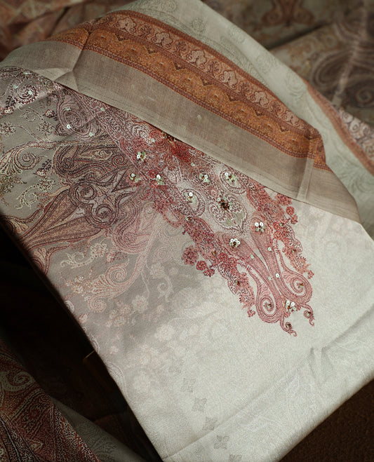 Beige colour churidhar material with subtle paisley motifs, sequin highlights, and woven border design, paired with a plain matching bottom and a soft printed dupatta for a graceful ethnic look.