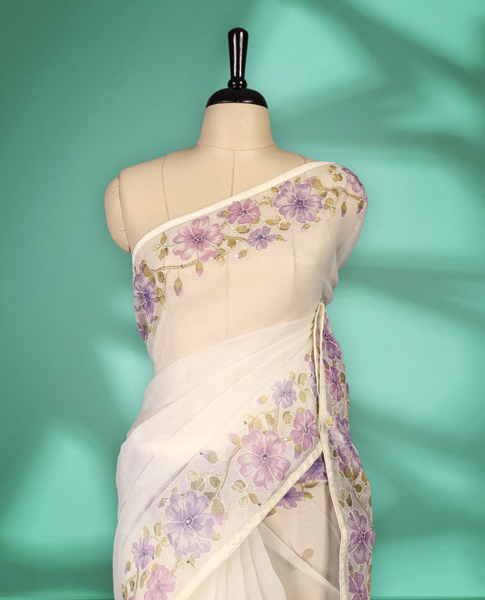 Ivory white colour organza saree adorned with purple floral print with thread detailing on the border and pallu, in a sheer finish that adds elegance, paired with a matching blouse for a graceful look.