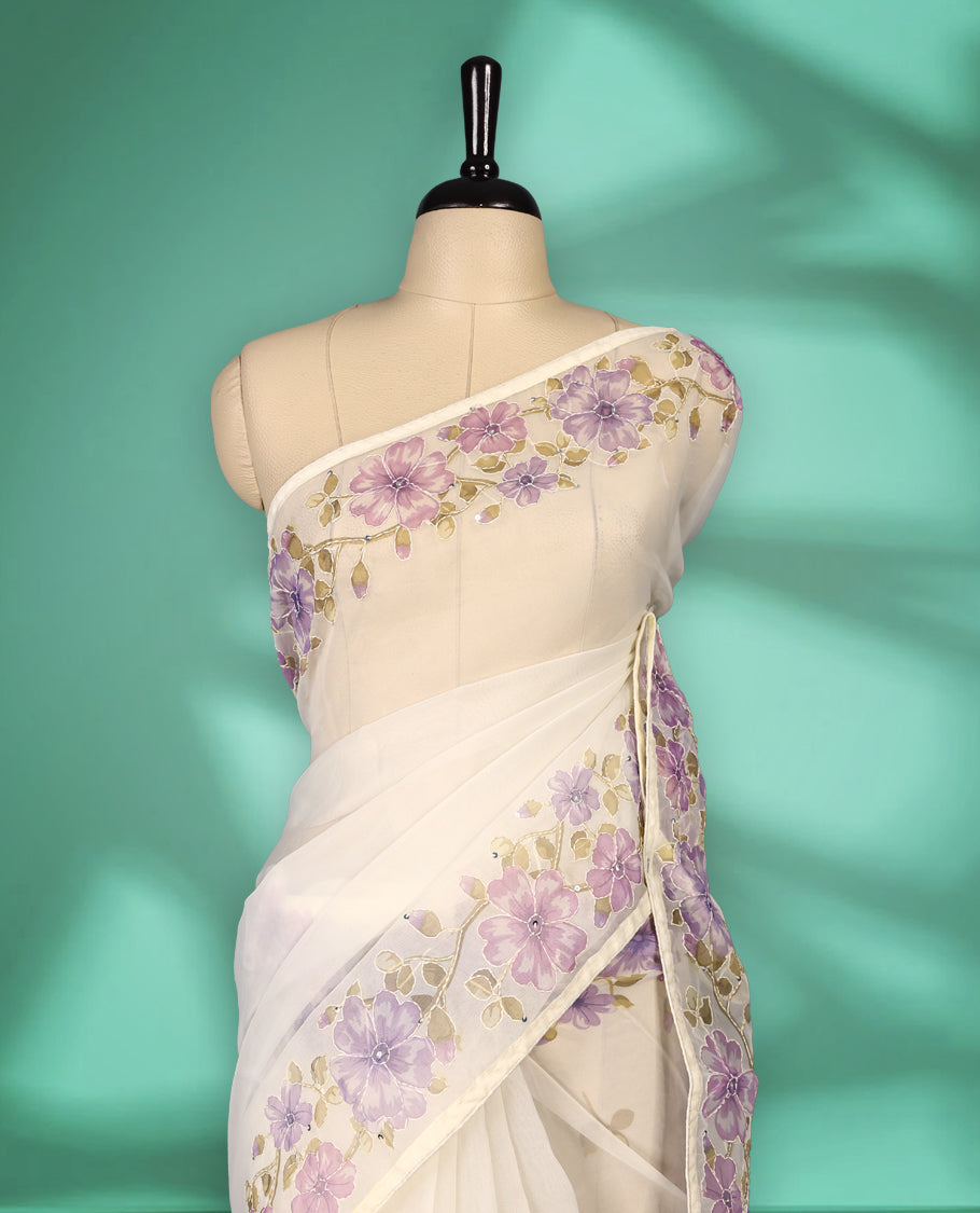 Ivory white colour organza saree adorned with purple floral print with thread detailing on the border and pallu, in a sheer finish that adds elegance, paired with a matching blouse for a graceful look.