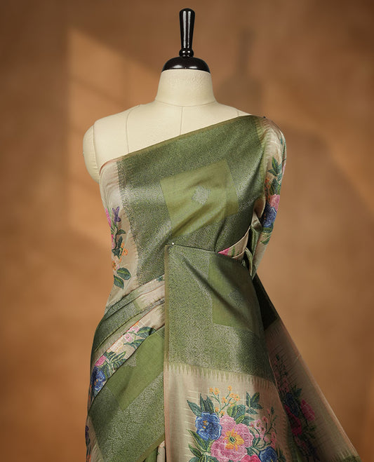 Green color semi tussar Banarasi saree featuring vibrant multi-color floral prints across the body, with shimmering geometric zari patterns, and a matching blouse detailed with silver woven buttas.