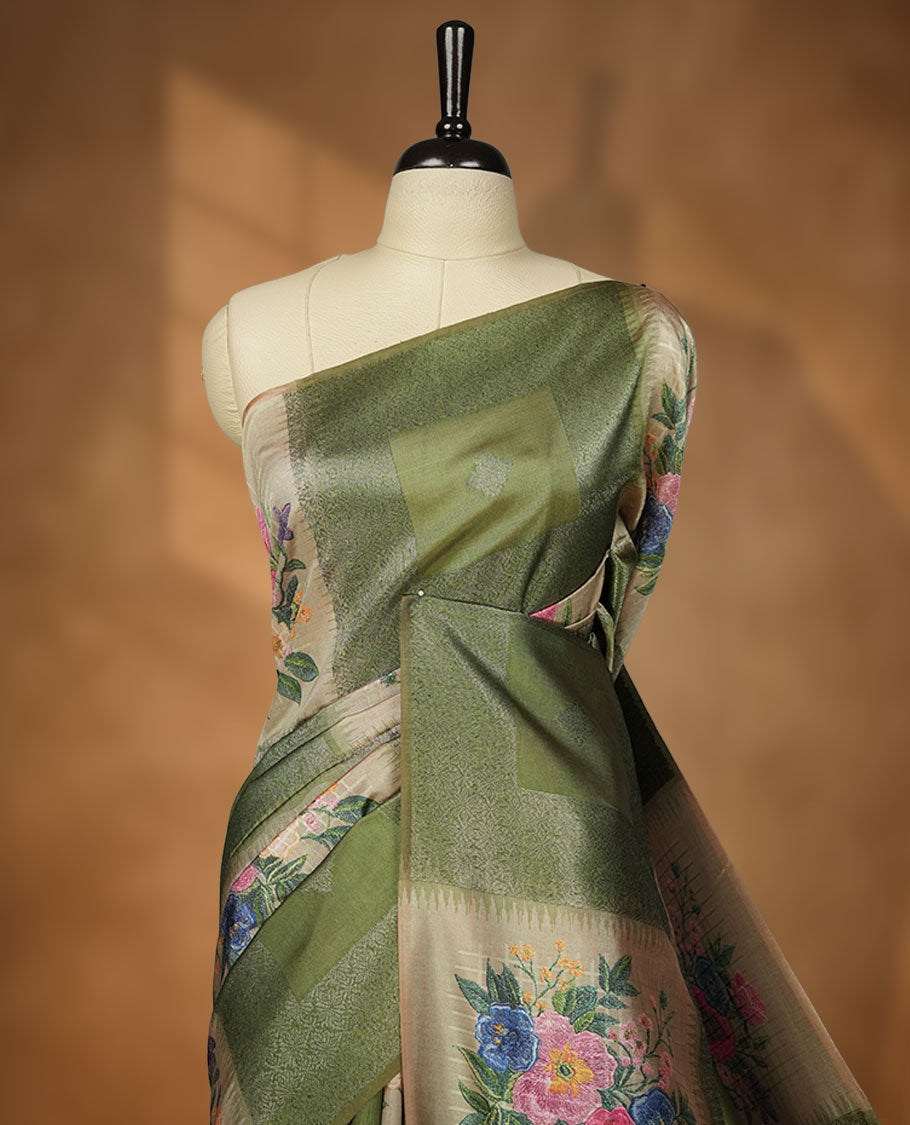 Green color semi tussar Banarasi saree featuring vibrant multi-color floral prints across the body, with shimmering geometric zari patterns, and a matching blouse detailed with silver woven buttas.