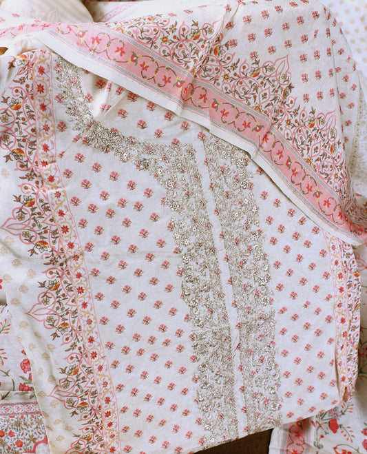 Cream colour churidhar material with delicate floral prints and intricate embroidery on the neckline, complemented by a printed dupatta and plain bottom.
