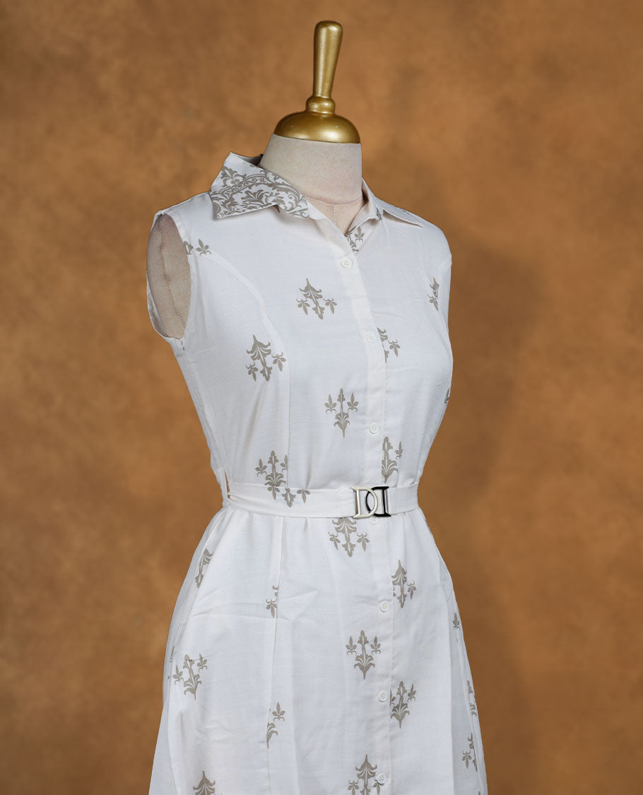 White sleeveless shirt dress with subtle grey ethnic motifs, front button placket, matching waist belt with metal buckle, and ornate border print at the hem.