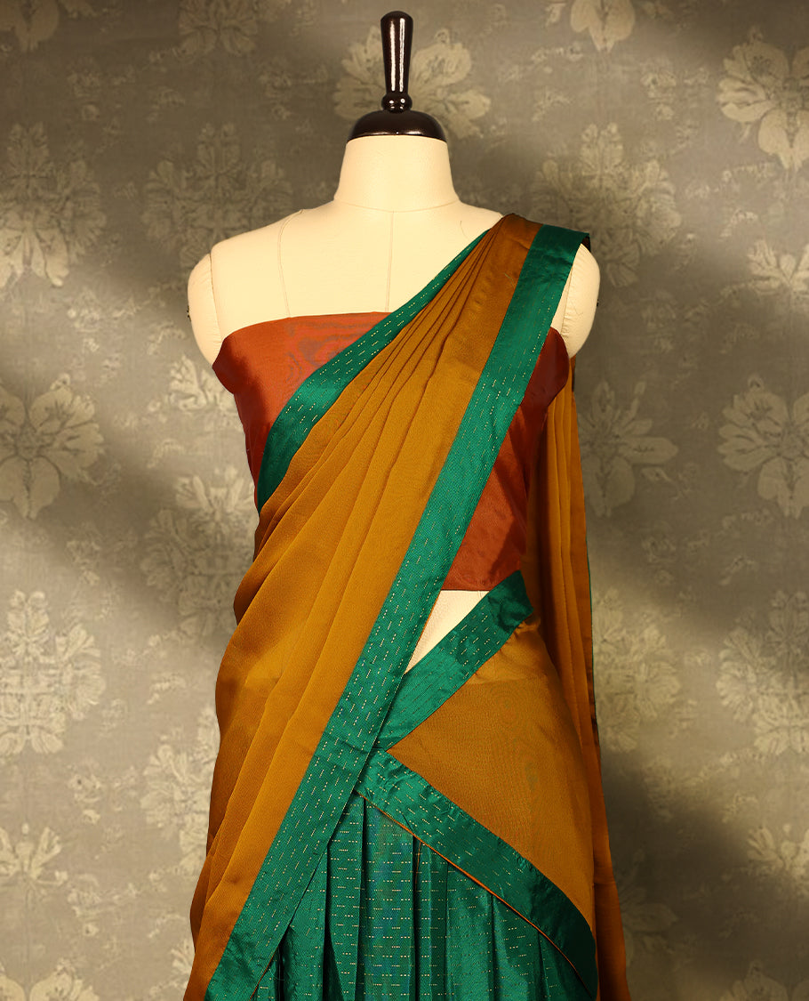 Green colour Semi Stitched  traditional half saree in semi Banarasi silk, featuring a Zari design with a Deep Orange bordered skirt. It is paired with a Rangoli georgette drape and comes with a blouse that matches the skirt’s border.