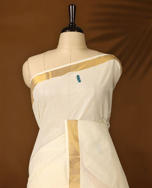 Elegant off white colour cotton Kerala saree featuring a golden zari border, colorful thread buttas, and vibrant peacock motifs on the pallu, and paired with matching blouse.