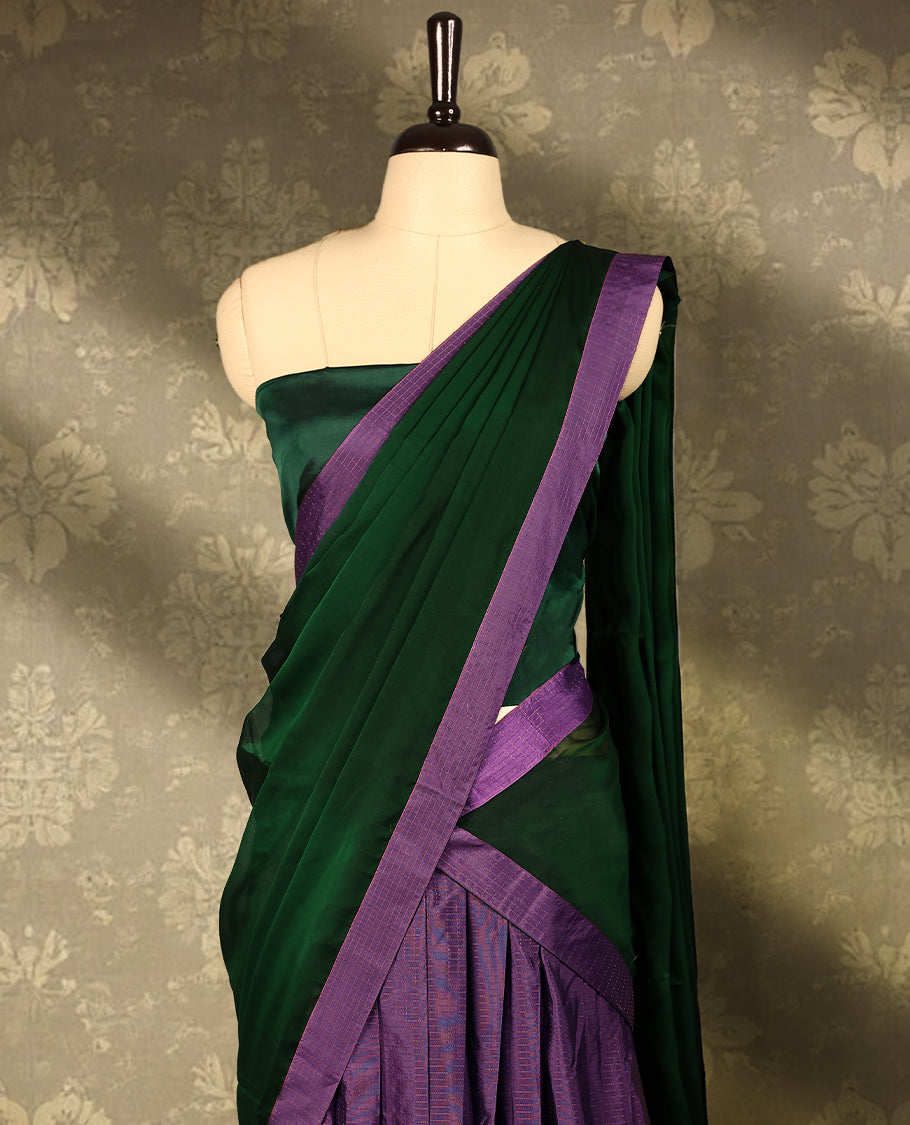 Lavender colour semi-stitched traditional half saree in semi Banarasi silk, featuring a checked design with a Bottle Green bordered skirt. It is paired with a Rangoli georgette drape and comes with a blouse that matches the skirt’s border.