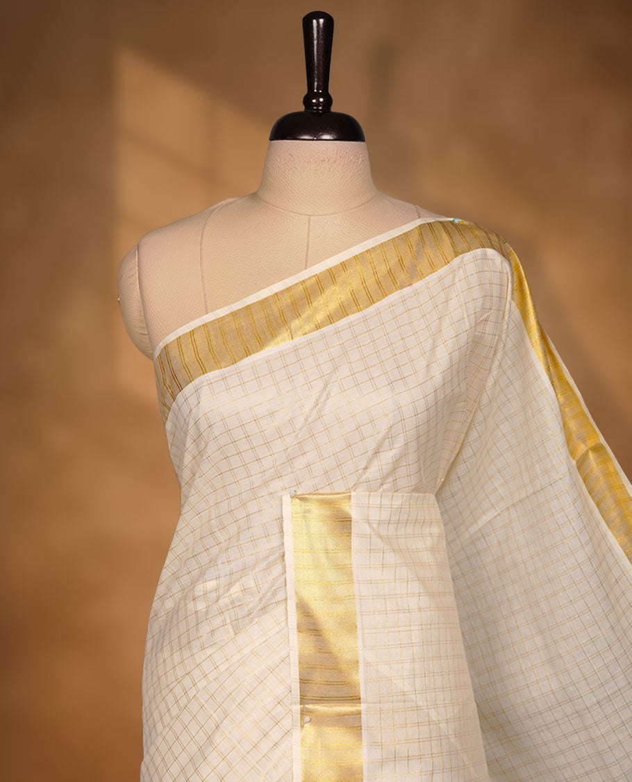 Off-white colour cotton Kerala saree featuring a subtle gold checkered weave, highlighted with a classic rich gold kasavu border along the edges and pallu, and paired with a matching blouse perfectly blending traditional charm with understated elegance.