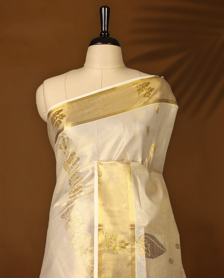 Elegant off white colour tissue Kerala saree featuring rich golden floral motifs and a shimmering zari border, exuding traditional charm and grace, Comes with a matching blouse to complete the timeless look.