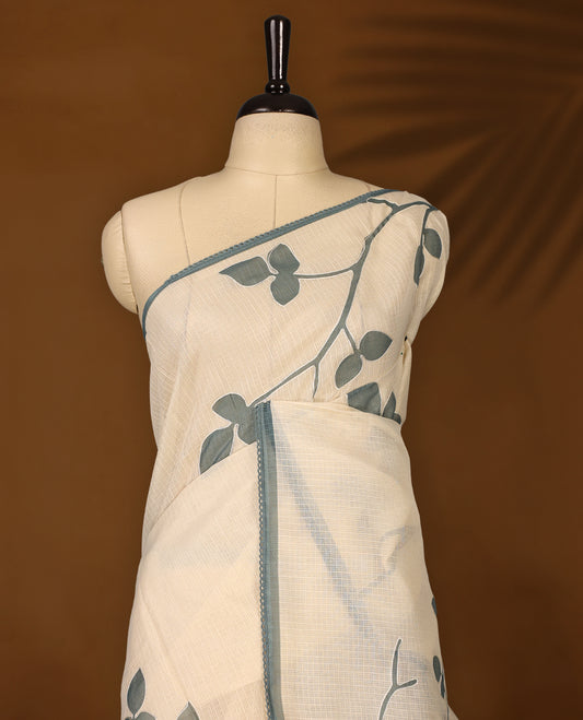 Cream colour Tussar cotton Kota saree featuring elegant stone blue leafy branch motifs across the body, accentuated with a subtle stone blue border, and paired with a matching blouse for a graceful and minimal look.