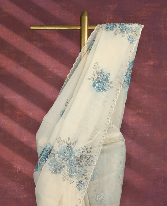 White colour pure organza saree featuring blue Colour floral prints with intricate bead and sequin work across the body, adorned with a matching embellished border, complemented by a worked pallu and paired with a heavily worked matching blouse.