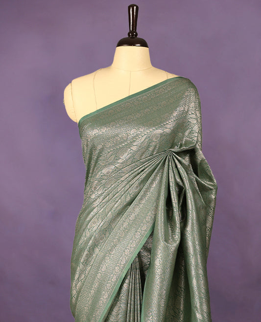 Pastel green colour semi Banaras Katan saree featuring an antique silver zari jacquard body, complemented by a self colour traditional border with a floral kodi design, paired with a matching blouse