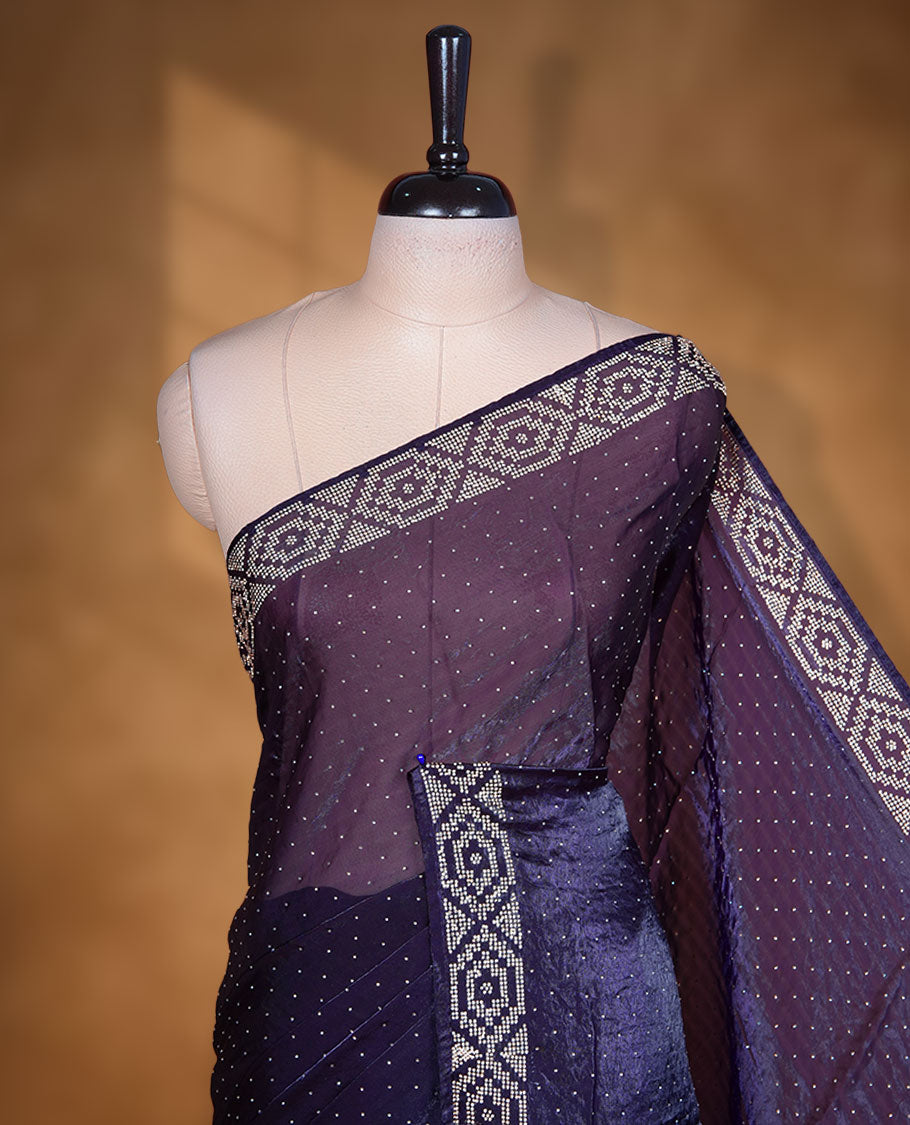 Dark purple colour chiffon designer saree, featuring delicate scattered stone detailing all over the body, highlighted with intricate stone work and a heavy geometric stone pattern along the border and pallu, paired with a matching embellished blouse.