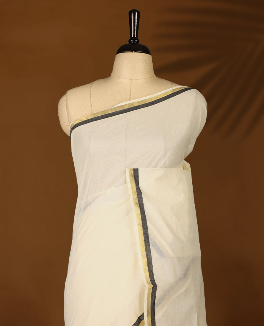 Elegant off white colour cotton Kerala saree featuring a plain body and traditional golden zari border with a hint of  Pure Black, offering a classic and graceful look, paired with a matching blouse.
