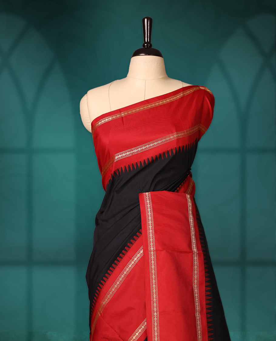 Black semi silk saree with plain body, vibrant red pallu and rich red border adorned with golden zari, accented with temple motifs along the edges, Paired with a matching blouse, perfect for festive occasions.