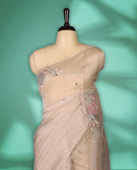 Beige Colour organza saree featuring delicate floral embroidery with applique, bead, mirror, and thread detailing on the body and scalloped border, lending a soft feminine charm, paired with a matching blouse.