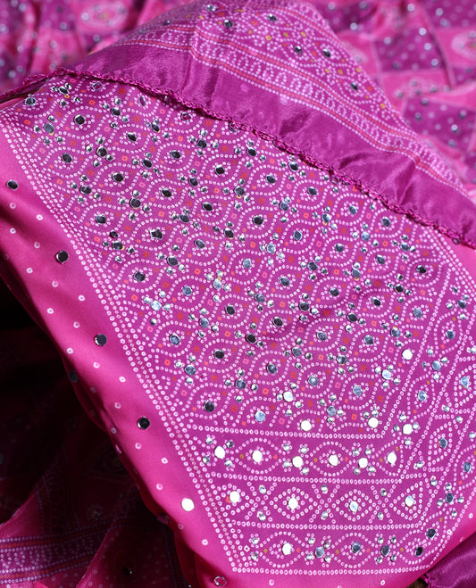 Magenta colour churidhar material adorned with intricate bandhani patterns and sparkling mirror work, paired with a plain matching bottom and elegant dupatta, perfect for festive gatherings and traditional celebrations.