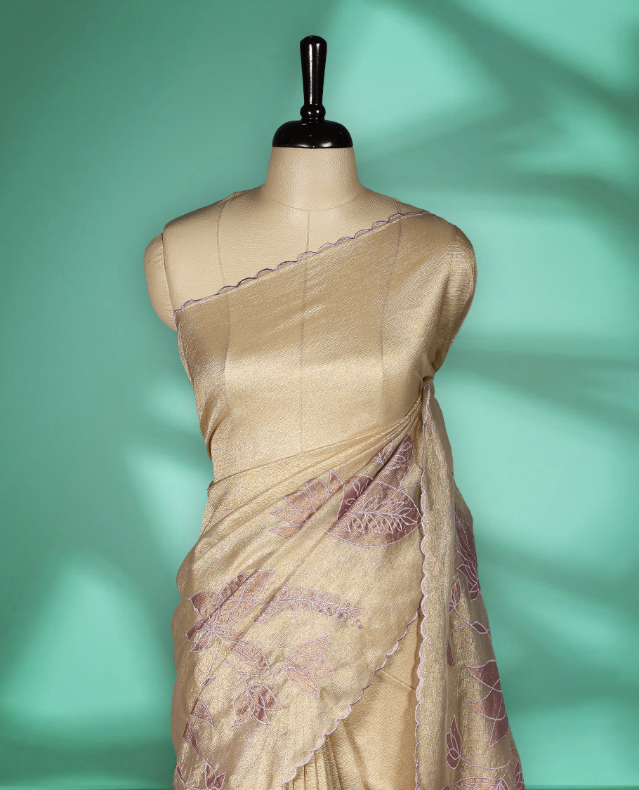 Champagne beige colour organza designer saree featuring subtle woven texture on the body, adorned with soft mauve floral embroidery along the border and pallu, finished with scalloped Thread edging paired with matching blouse.