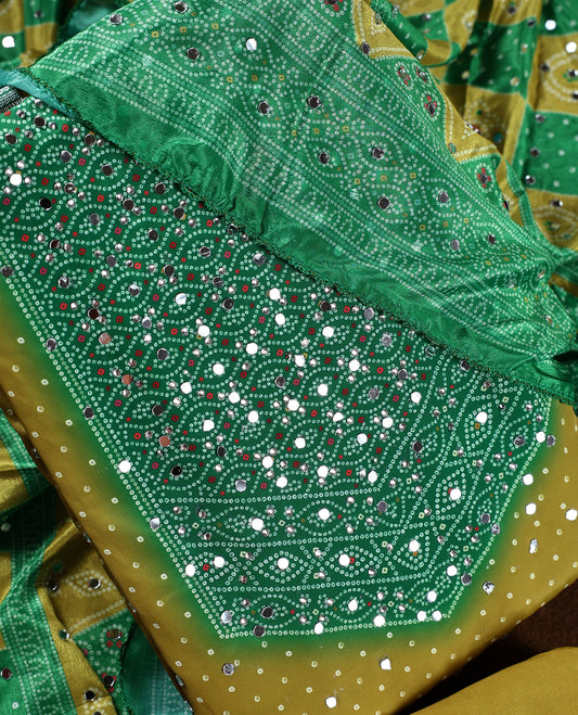 Lemon green colour churidhar material with intricate Bandhani style patterns and sparkling mirror work, Paired with a plain mustard bottom and a matching dupatta highlighted with mirror embellishments.