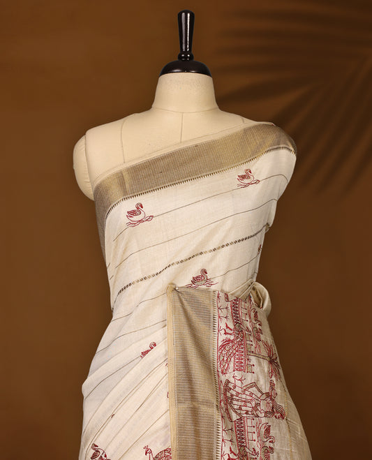 Cream colour Soft Tussar saree featuring fine golden woven stripes across the body, accentuated with maroon village and temple motifs on the pallu, finished with a rich golden zari border, paired with a matching blouse.