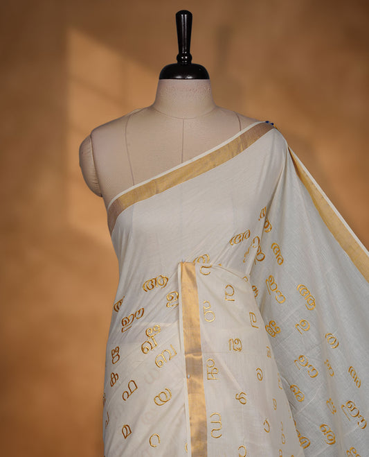 Off-white colour cotton Kerala saree, featuring a classic gold kasavu border and delicate gold-toned Malayalam script motifs woven across the body and pallu. paired with a matching blouse