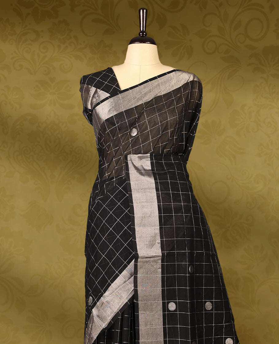 Black colour pure handloom cotton kerala saree with white checkered pattern and silver woven buttas on the body, silver zari border, pallu detailed with silver zari stripes and buttas, with matching blouse